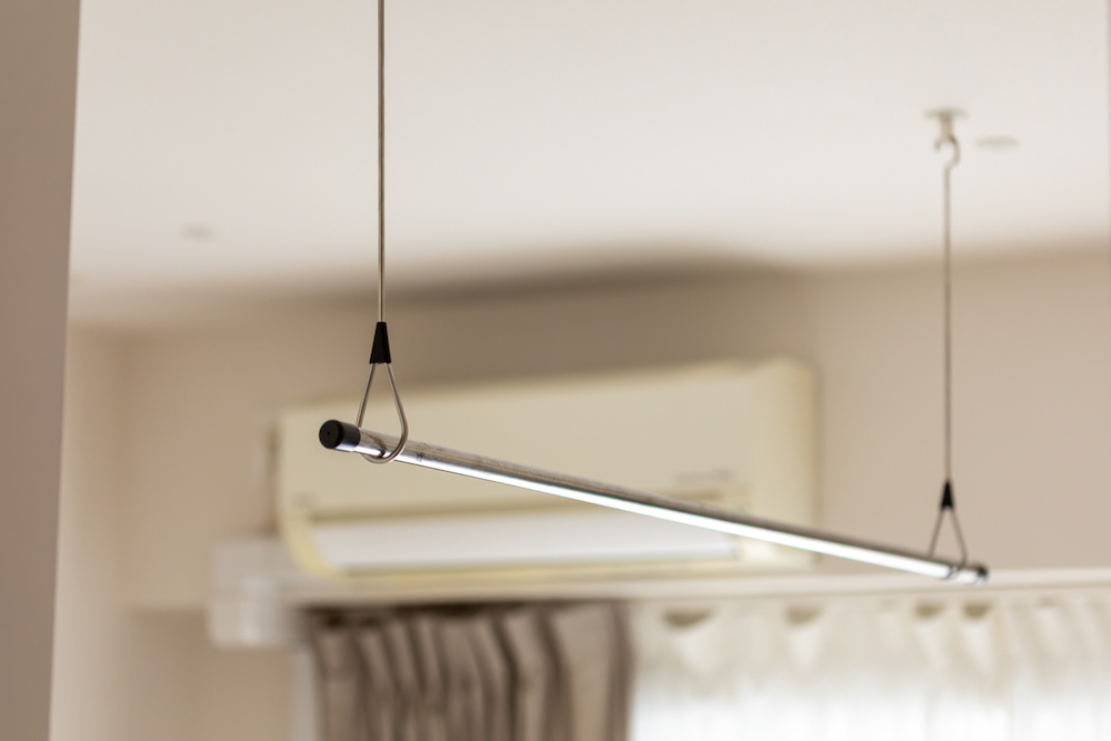 エアコンの風が当たる位置に設置された、天井吊り下げ型の室内物干し(ホスクリーン)のリノベーション事例。インテリアに馴染むスタイリッシュなステンレス製の物干し竿。