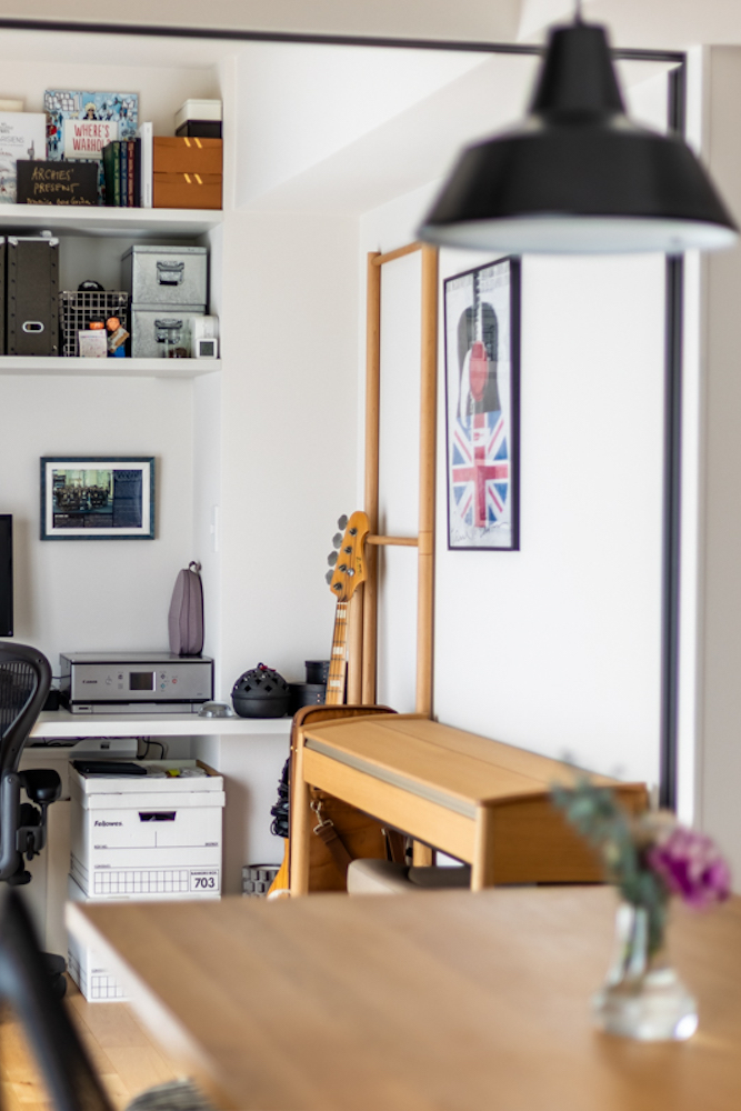 リビングダイニングとつながるように設けたワークスペースのリノベーション事例。造作デスクと壁面収納棚に、ベースや木製ピアノなどの趣味のアイテムが並ぶ空間