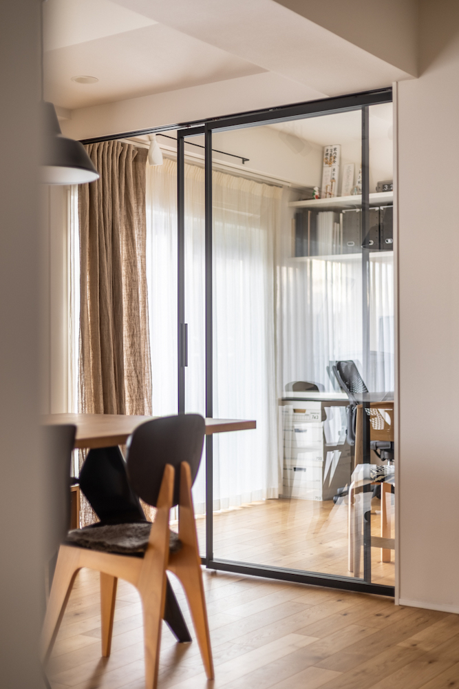 ダイニングと奥のワークスペースを仕切る、黒いフレームのガラス引き戸のリノベーション事例。光を通しつつ空間を分ける抜け感のある間取り