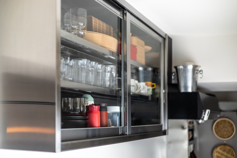 ステンレスフレームとガラス引き戸を採用したキッチン吊り戸棚のリノベーション事例。お気に入りのグラスや食器を見せる収納に