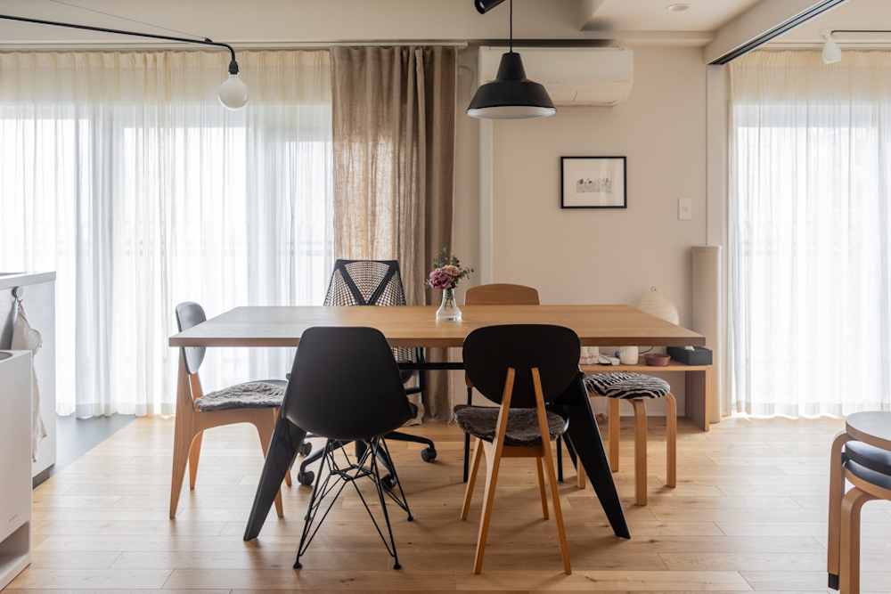 ナチュラルな木目調フローリングと大きな窓からの採光が明るい、ダイニングのリノベーション事例。広めの木製テーブルに、異なるデザインのチェアや黒いペンダントライトを合わせたミックススタイル