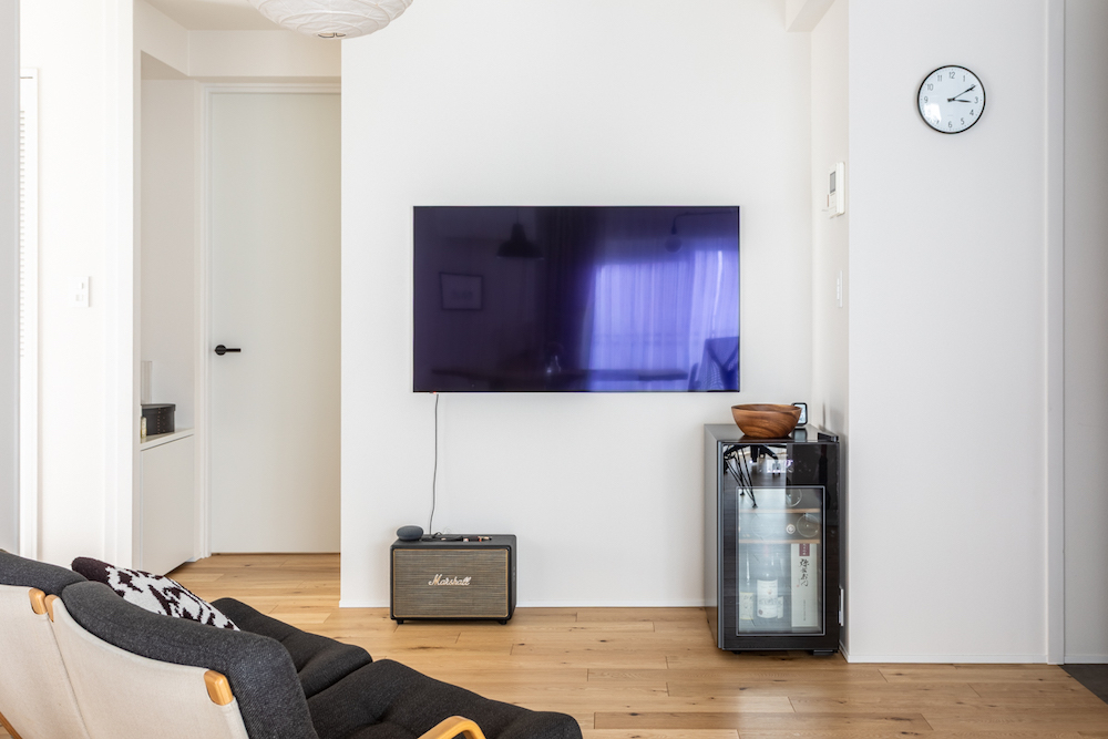 テレビを壁掛けにして配線をすっきりさせた、シンプルで洗練されたリビングのリノベーション事例。足元にはMarshallのスピーカーや小型のワインセラーを配置。
