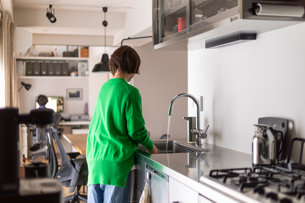 ダイニングや奥のワークスペースまで見渡せるキッチンのリノベーション事例。ステンレス天板とアーチ型の水栓を採用し、家族の気配を感じながら家事ができる間取り。