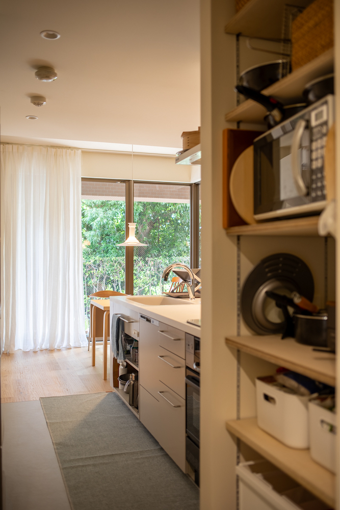 手前に電子レンジなどが並ぶオープン収納、奥には庭の緑が見える明るいキッチンの風景。