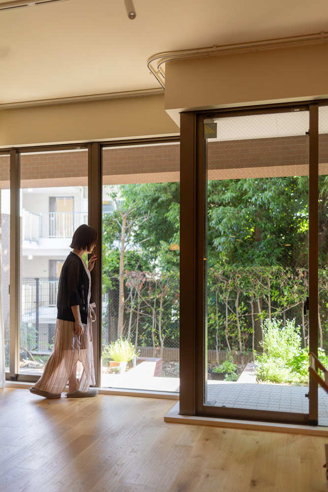 リビングの大きな掃き出し窓の前に立ち、外の緑豊かな庭を眺めている女性